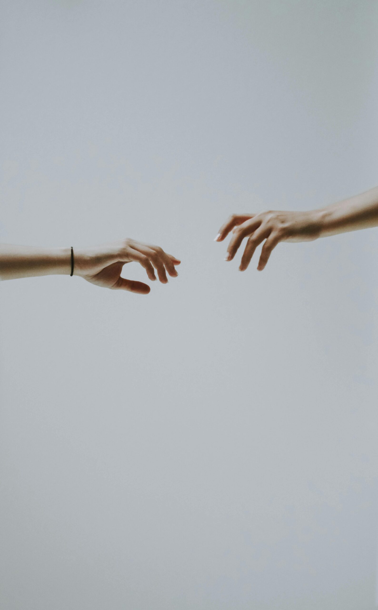 A minimalistic photo of two hands reaching out to each other against a soft, neutral background.